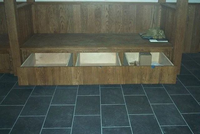 Wooden shelf with three open bins against a wall, above dark tiled flooring.