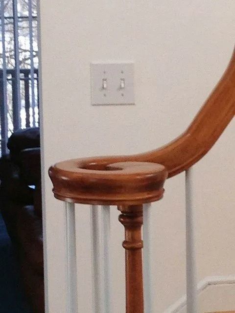 Wooden stair railing and white wall with a light switch near a staircase landing