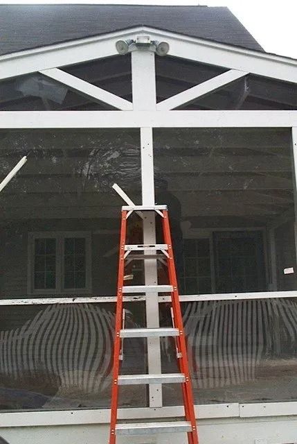 Red ladder leaning against a house porch with dark siding and white trim
