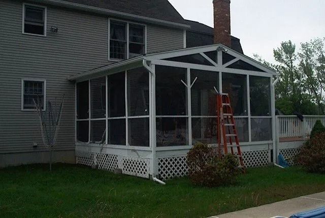 Screened porch attached to a gray house, with a red ladder leaning inside and a brick chimney.
