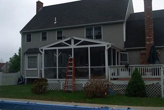 Backyard view of a gray two-story house with a screened porch, red ladder, and an above-ground pool