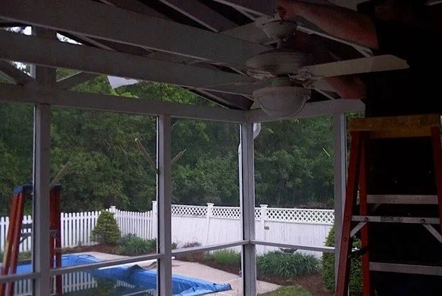 Partially built porch ceiling with exposed beams, a red ladder, and a backyard pool beyond a white fence