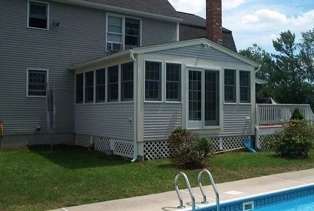 Screened porch beside a house, next to an outdoor swimming pool on a sunny day.