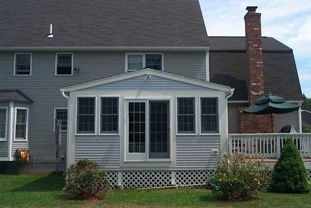 Gray house with a small enclosed porch, white trim, brick chimney, and front lawn.