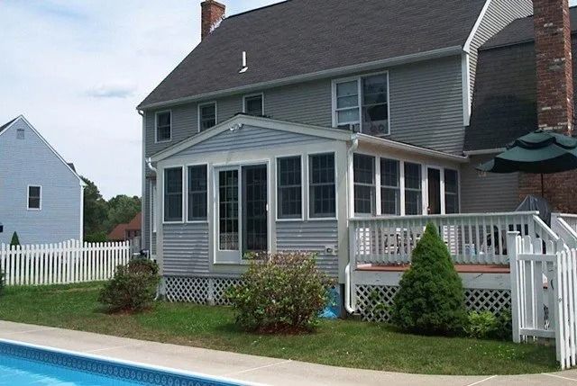 Gray two-story house with white porch and fenced backyard beside a swimming pool