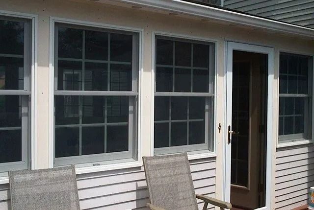 Exterior of a house with white siding, large windows, and a partially open door beside patio chairs