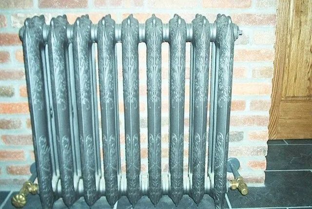 Old cast-iron radiator against a brick wall beside a wooden cabinet.