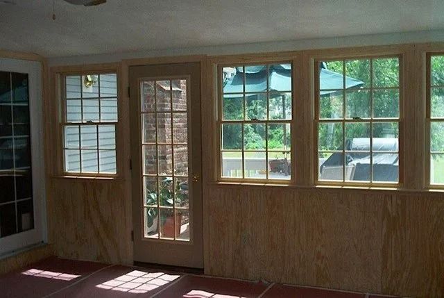 Empty sunroom with wood-paneled walls, large windows, and a glass door letting in daylight.