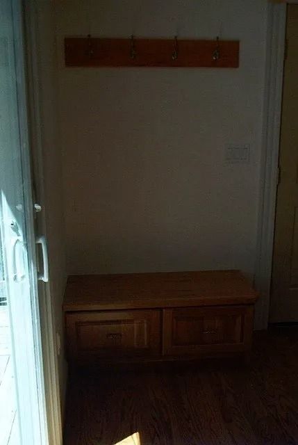 Dim hallway with a wooden bench, wall hooks, and sunlight from the left.