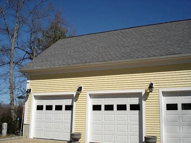 Yellow house with three white garage doors under a gray roof on a sunny day