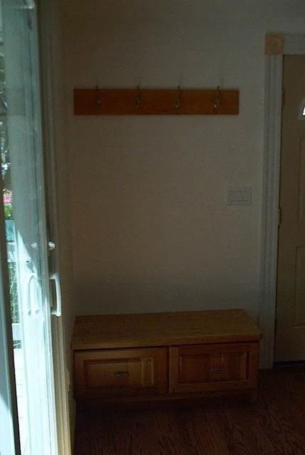 Hallway with wooden bench and wall-mounted coat rack, near a doorway and window blinds