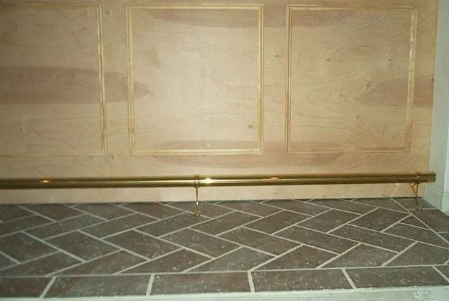 Stone fireplace hearth with brass rail and beige paneled wall above it