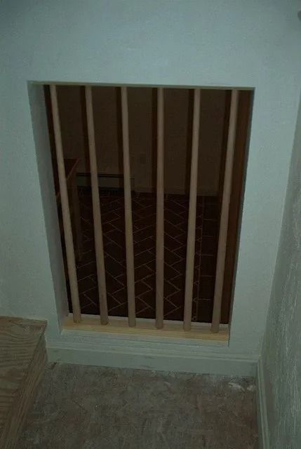 Small barred opening in a wall with a view into a dim room behind it.