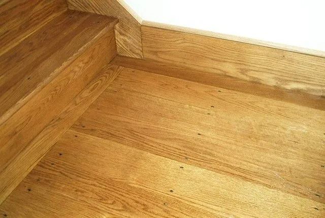 Wooden staircase corner with matching hardwood floor and white wall trim