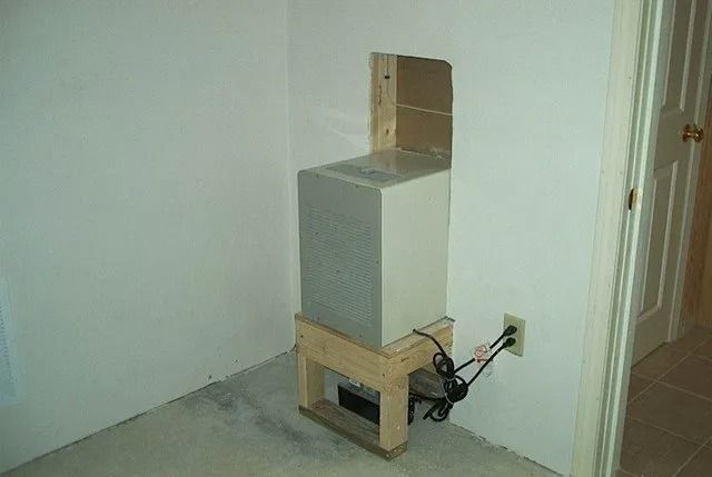 Gray box on a wooden stand in a bare room, with cords plugged into the wall.