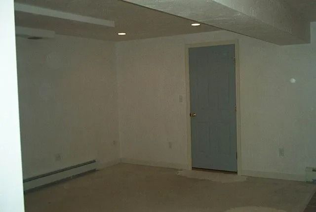 Empty beige room with a closed gray door and low ceiling lights