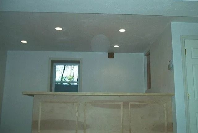 Empty room with white walls, recessed lights, a small window, and a wooden bar or counter.