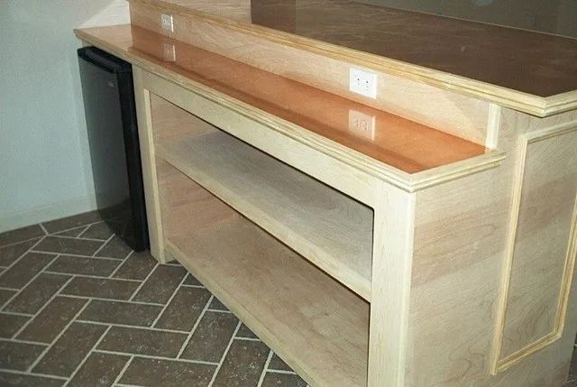 Light wood built-in cabinet or bench with shelves and bench seat in an indoor room, beside a trash bin