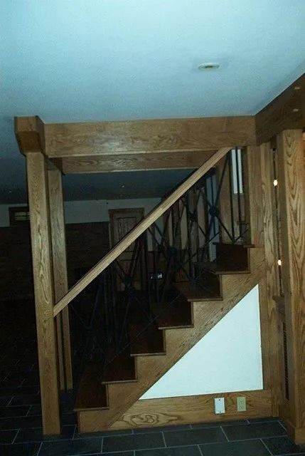 Wooden staircase with dark balusters and unfinished plywood walls in a dim interior room