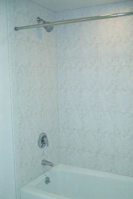 White tiled bathroom with a bathtub, showerhead, and curtain rod.