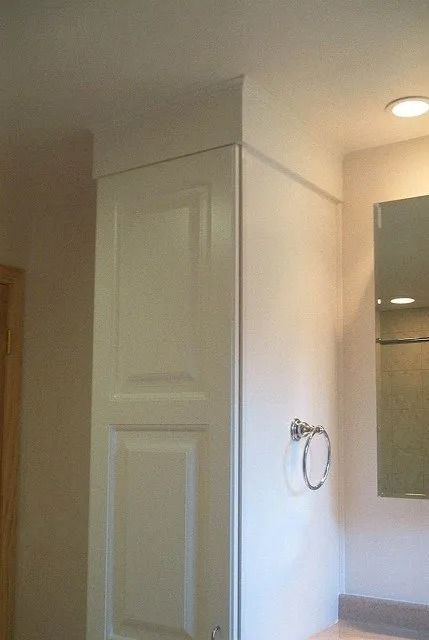 Bathroom with a white cabinet, towel ring, mirror, and shower area under warm ceiling light