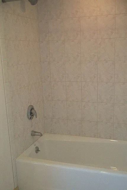 Empty bathtub against beige tiled bathroom wall