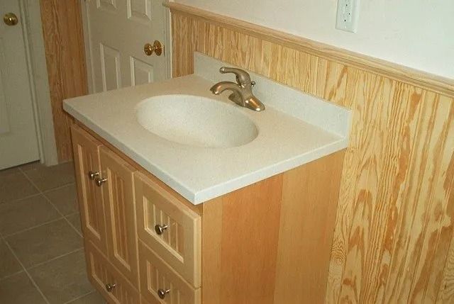 Small bathroom vanity with white sink, beige countertop, and wood cabinets against a paneled wall