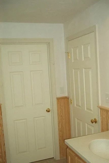 Small bathroom with two white paneled doors, wood trim, and a sink in the corner.
