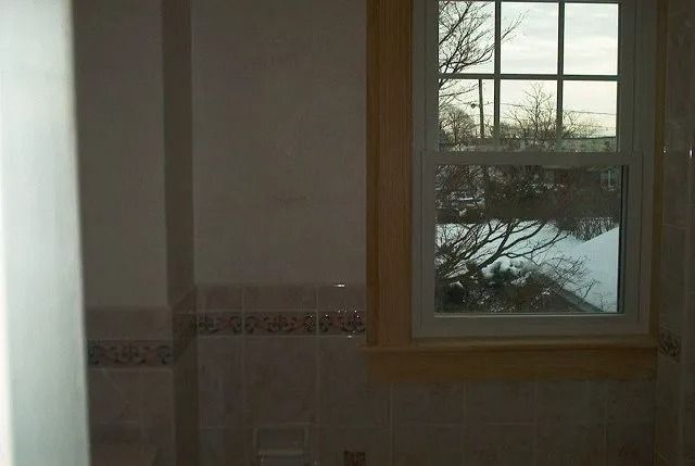 Dim bathroom interior with tiled wall and a window showing trees outside