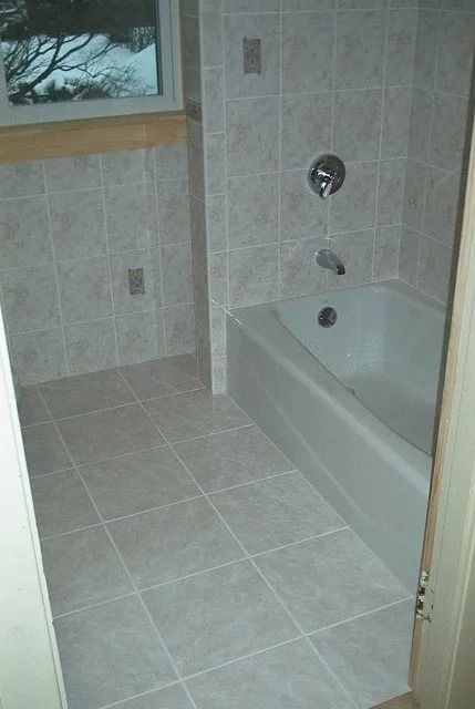 Small tiled bathroom with a bathtub, wall-mounted faucet, and window.