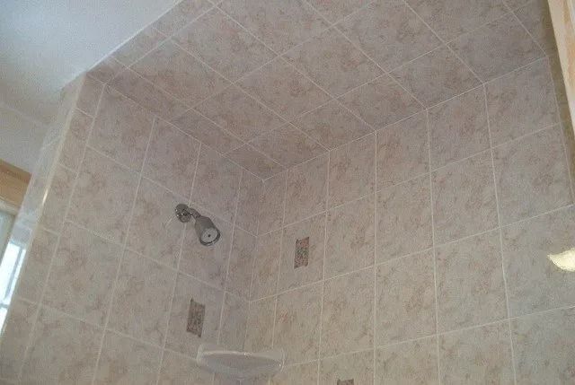 Tiled shower stall with wall-mounted showerhead and small shelf in a corner.