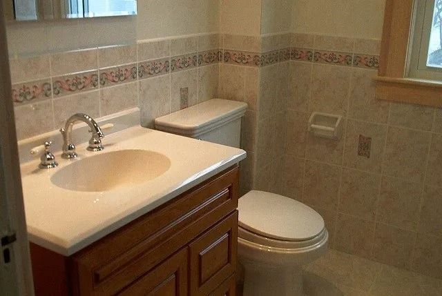Bathroom with beige tile, white sink, toilet, and wooden vanity under a window.