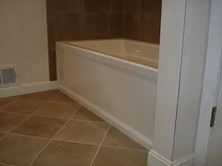 Empty bathroom with a white bathtub, brown tile walls, and beige tiled floor.