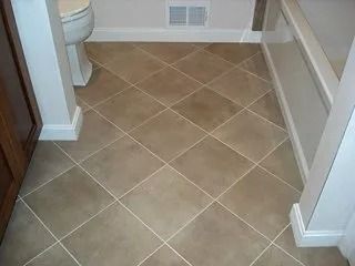Small bathroom with beige diamond-tile floor and white fixtures near a toilet and shower.