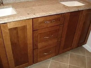 Wooden bathroom vanity with granite countertop, two sinks, and central drawers.