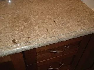 Brown marble countertop above wooden drawers with curved metal handles