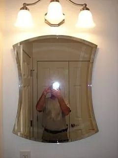 Bathroom mirror with person taking a flash photo beneath a three-light vanity fixture