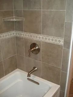 Corner of a tiled shower with a bath shelf and wall-mounted faucet above a tub, in beige and white tiles