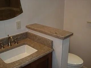 Bathroom vanity with stone countertop, white sink, and toilet beside a half wall.