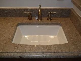 Bathroom sink with beige countertop and white basin, centered beneath brass faucet handles.