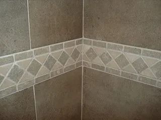 Brown tiled bathroom corner with a decorative white and gray mosaic border