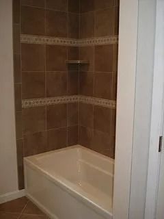 Bathtub alcove with brown tiled walls and a small corner shelf.