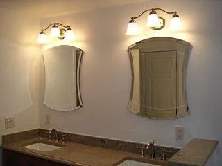 Bathroom vanity with two lit wall sconces, mirrors, and a granite countertop