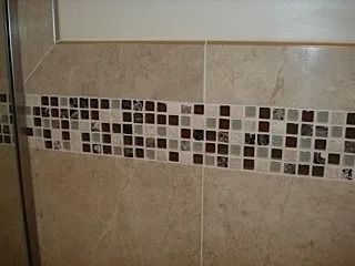 Beige tiled wall with a horizontal strip of small brown, white, and green mosaic tiles.