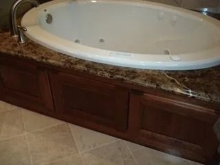 Oval bathtub set into a dark wood bathroom vanity with a granite countertop and tile floor