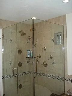 Glass-enclosed shower with beige tile walls and decorative mosaic border