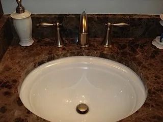 White oval bathroom sink with bronze faucet and dark marble countertop