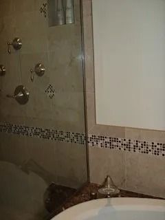 Bathroom shower with beige tile, glass door, and a small cat resting on the floor near the corner
