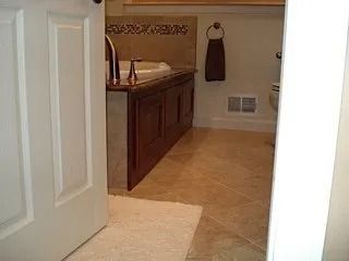 Open bathroom doorway with vanity, tan tile floor, and wall vent.