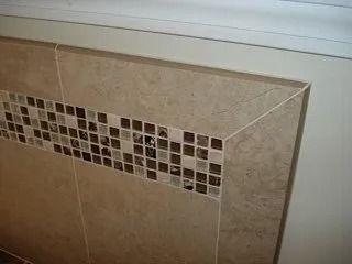 Beige tiled wall with a horizontal mosaic accent strip below a white ledge
